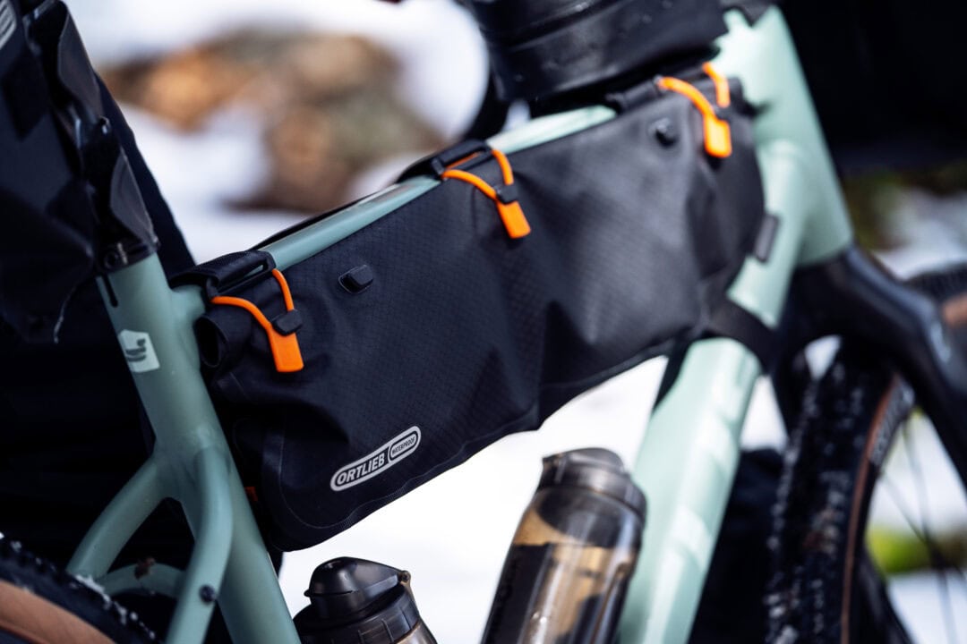 Close-up of a mint-green bike frame with a black Ortlieb waterproof bag attached and orange zipper pulls prominent on the bag edge.