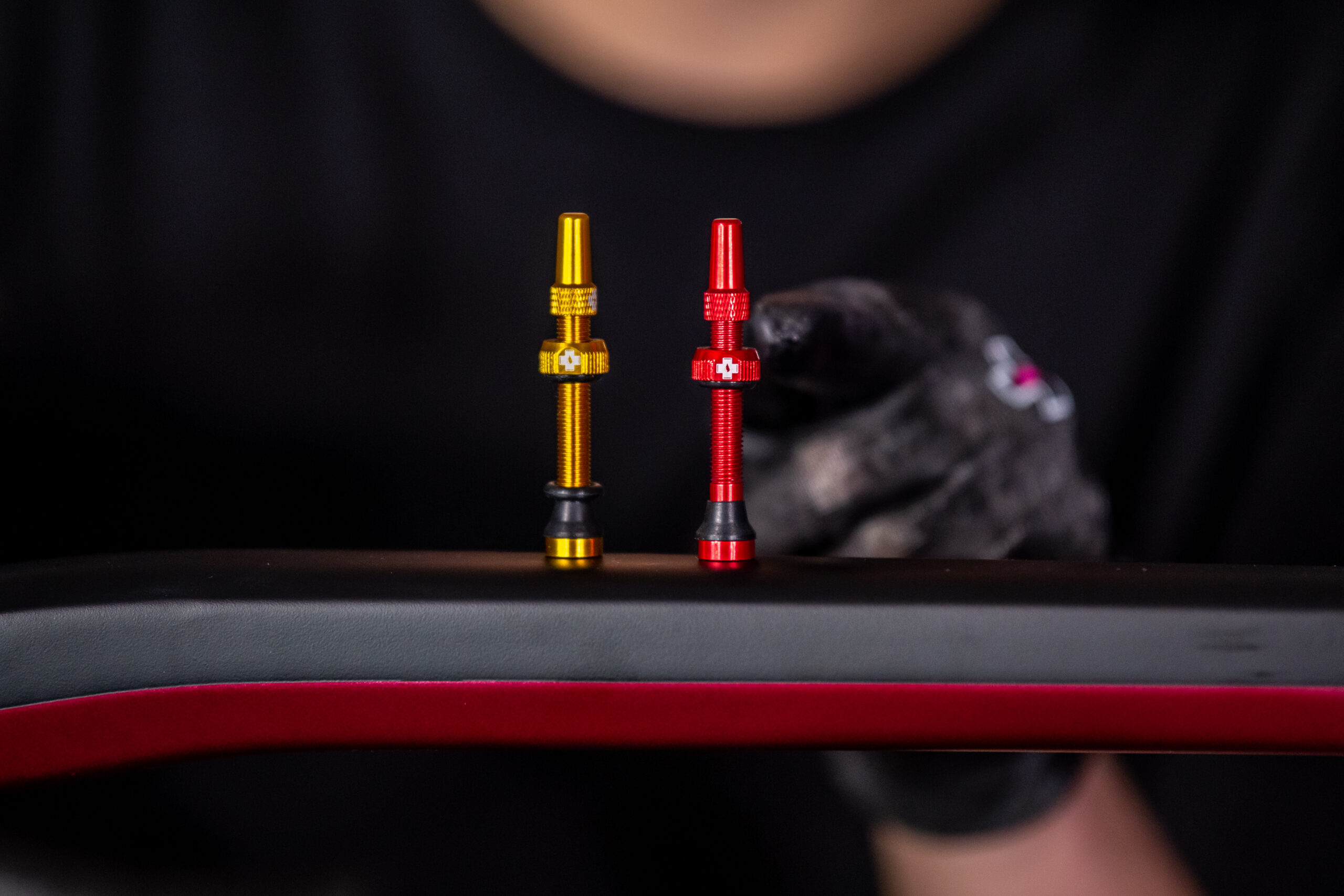 Two anodized gold and red valve stems with knurled grips, standing upright on a dark surface.