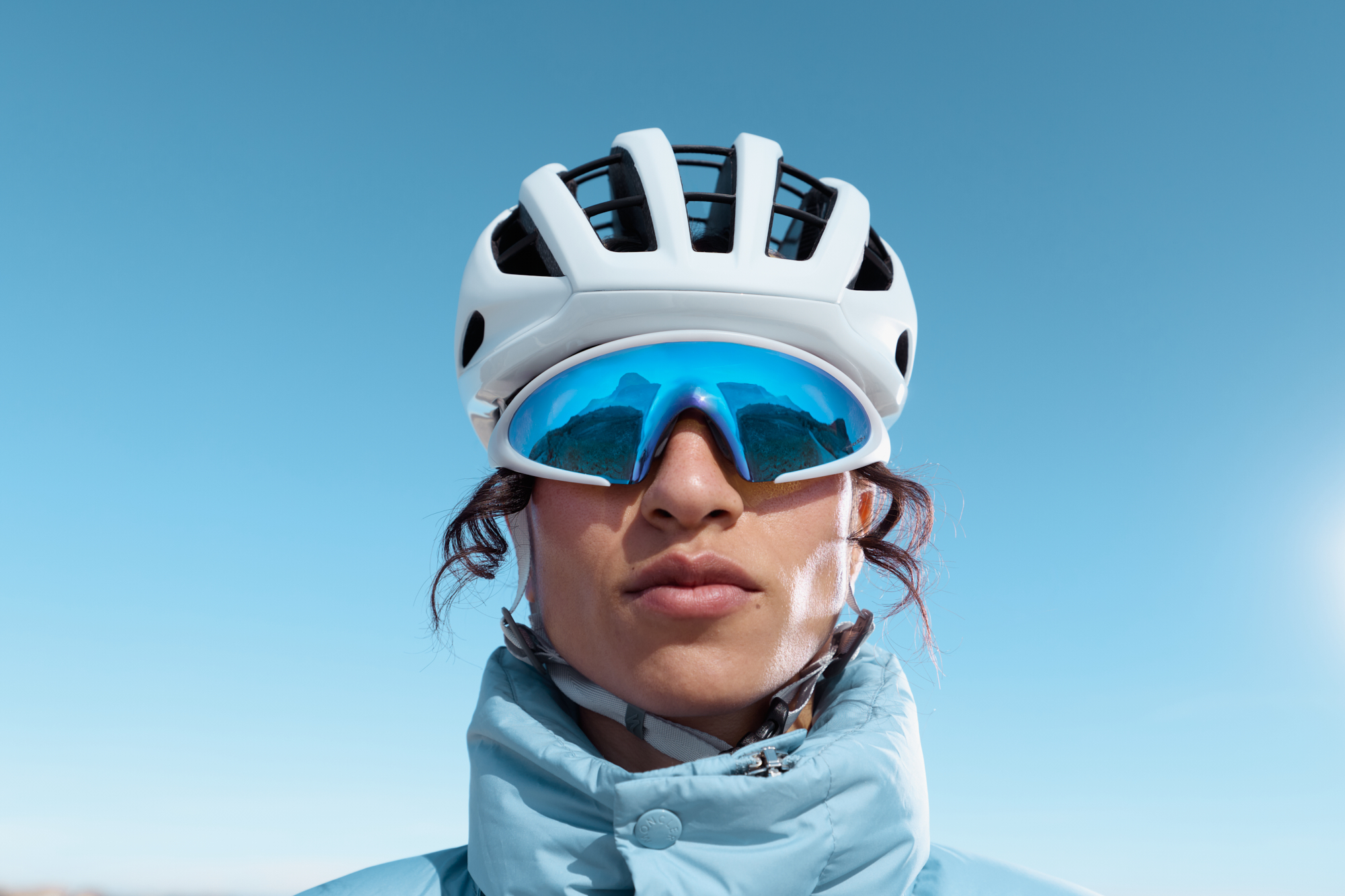 Close-up of a cyclist wearing a white helmet and blue mirrored sunglasses against a clear blue sky