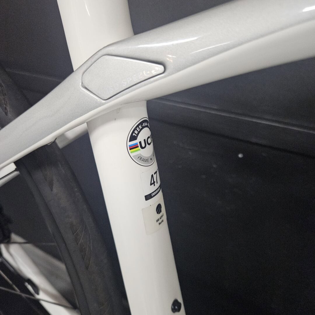Close-up of a white bicycle frame joint with a badge showing UCI and rainbow stripes stickered on the tube.