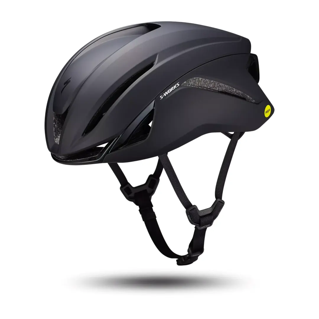 Matte black S-Works bicycle helmet with MIPS yellow sticker and adjustable chin straps, shown in midair above a shadow.