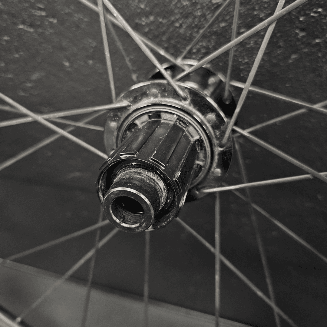 Close-up of a bicycle wheel hub with spokes radiating outward against a dark background, showing the metal bearings and cap at the center.
