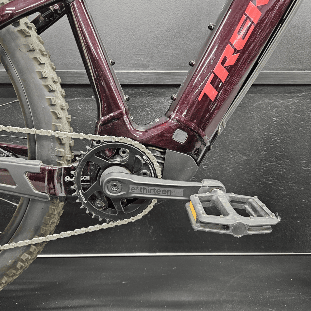 Close-up of a maroon mountain bike frame with chainring, crank, and pedals visible.