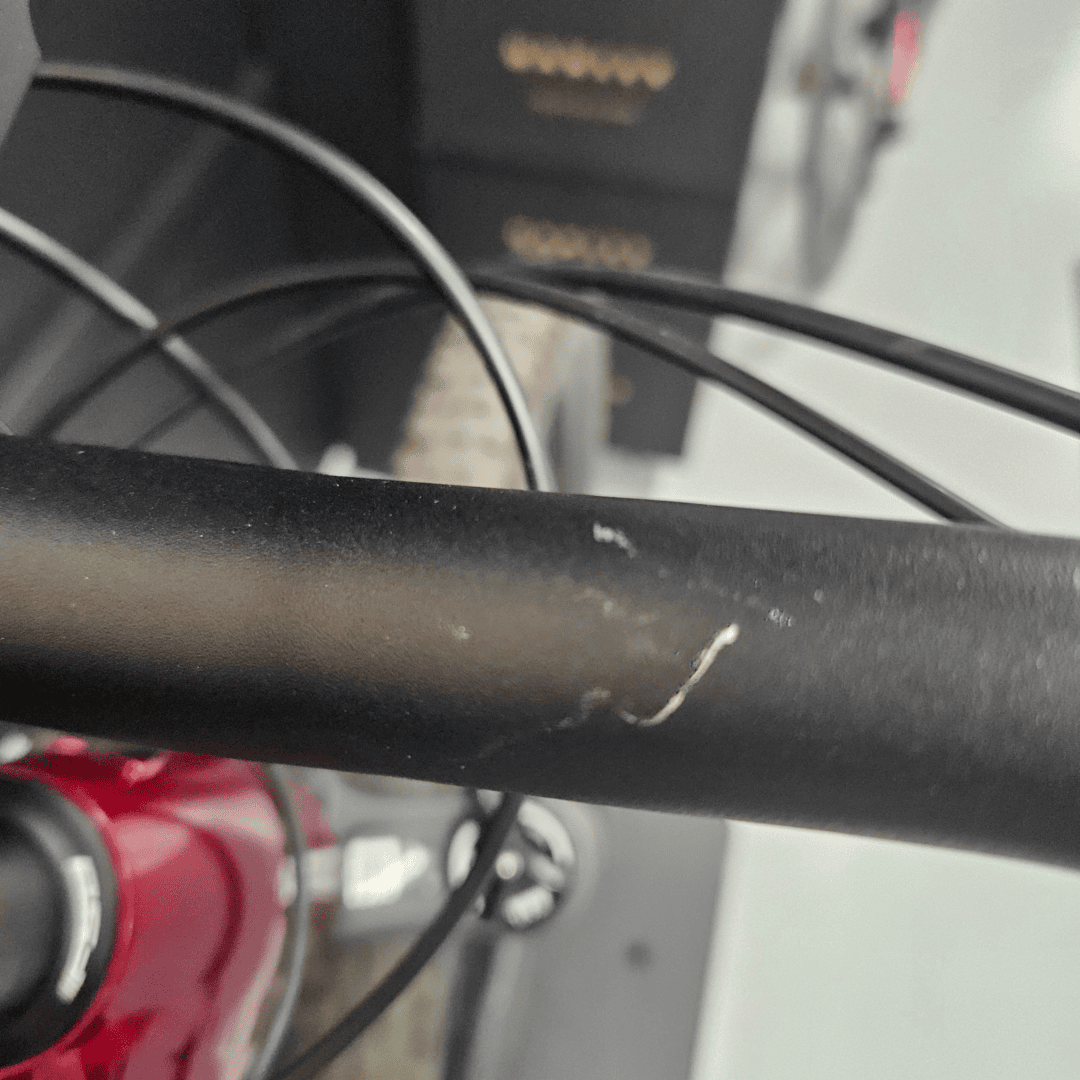 Close-up of a red bicycle frame with black cables crossing in front and a blurred background edge of a wheel.