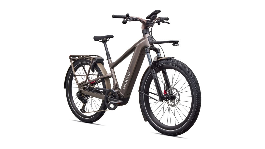 Brown Specialized electric mountain bike with fat tires, front suspension, and a rear rack on a white background.