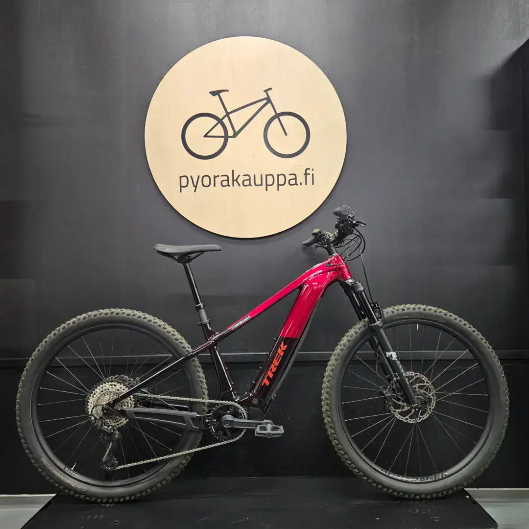 Red mountain bike on display against a dark wall, with a large round wooden sign reading 'pyorakauppa.fi'.