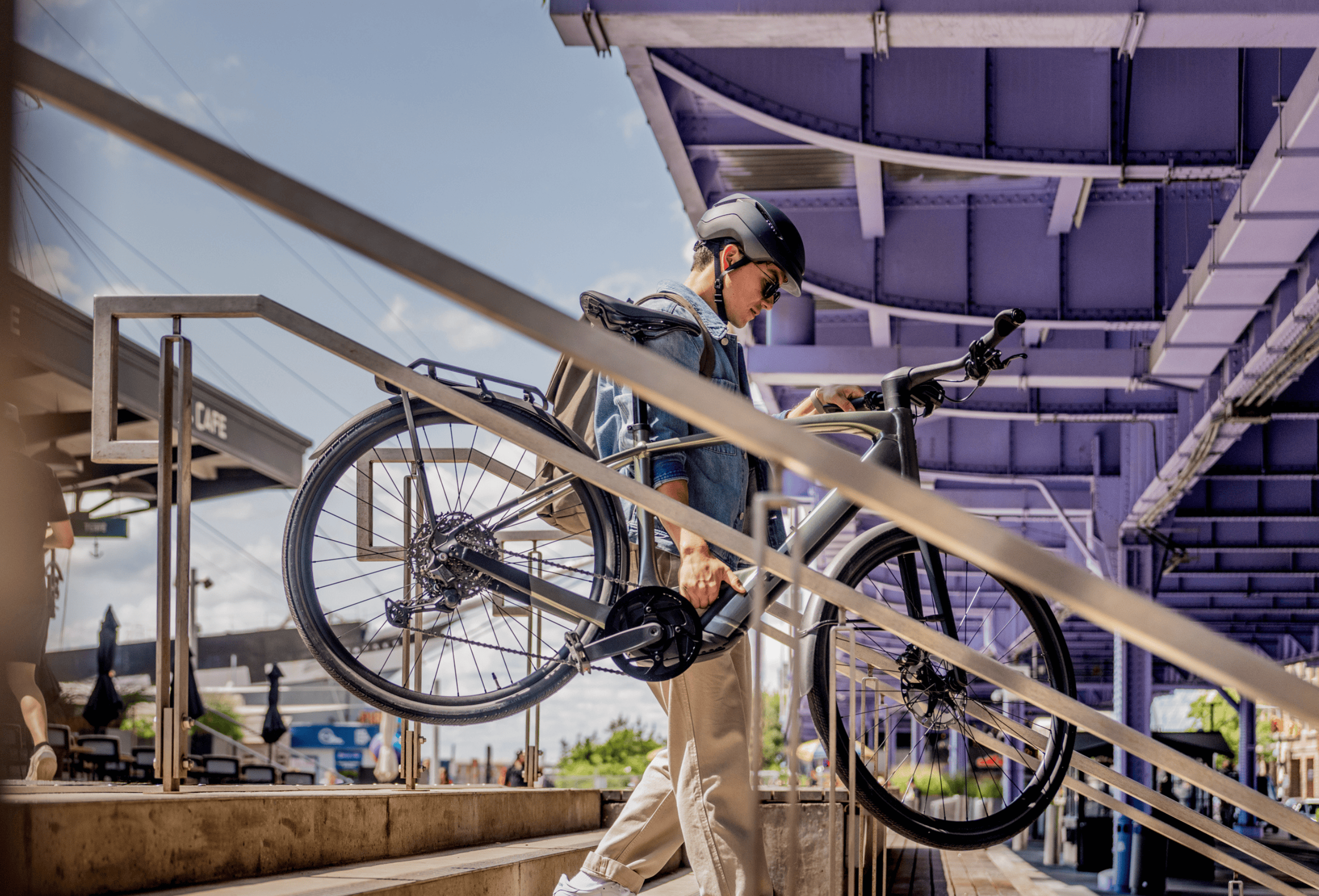 Person with a helmet adjusting a green bike on an outdoor ramp under a purple bridge.