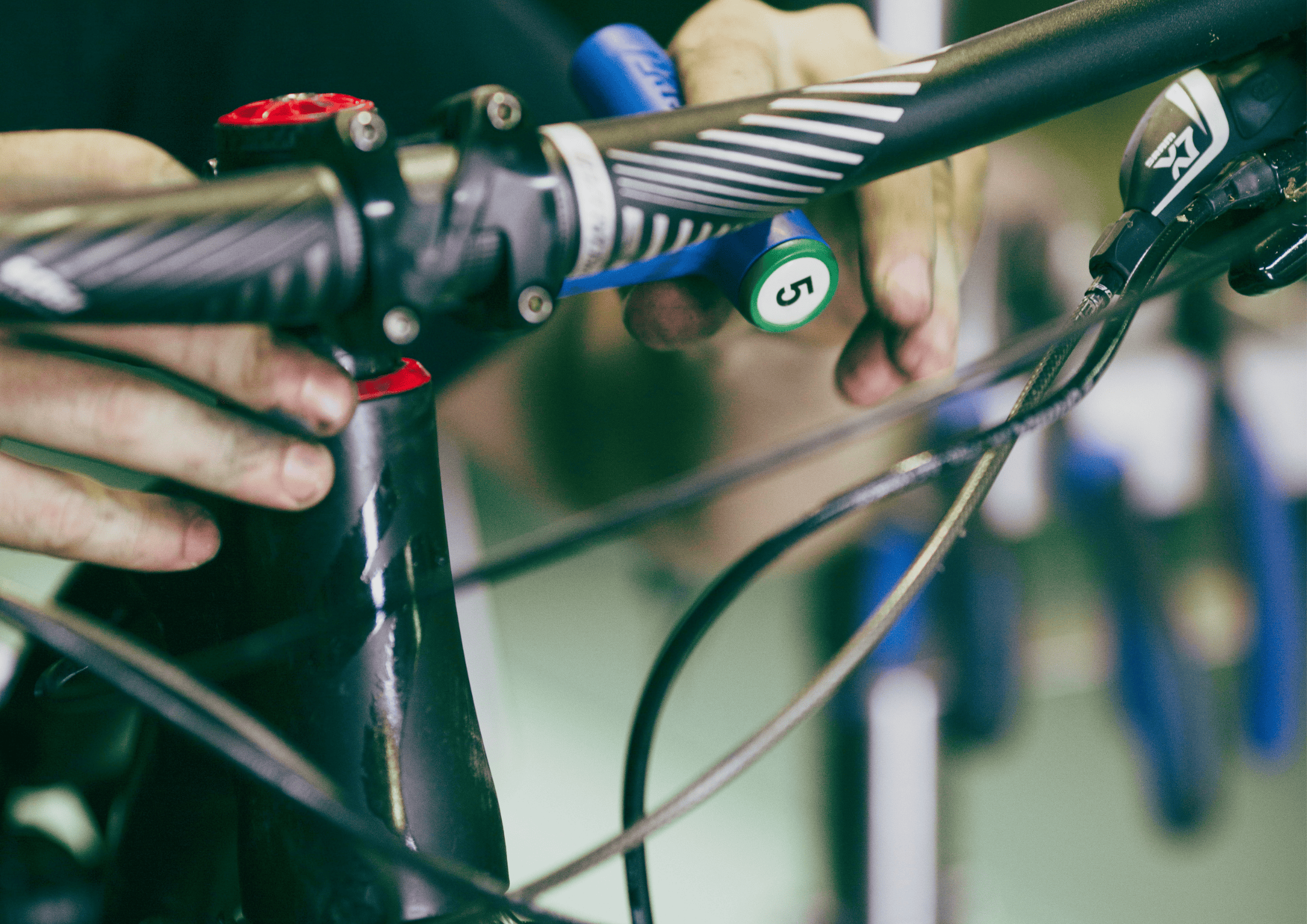 Close-up of a mechanic's hands adjusting a bicycle handlebar and stem with blue spacers visible.
