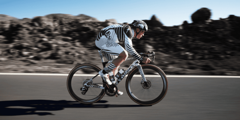 Cyclist in zebra-striped kit riding a road bike at speed on a sunny day with a blurred background.