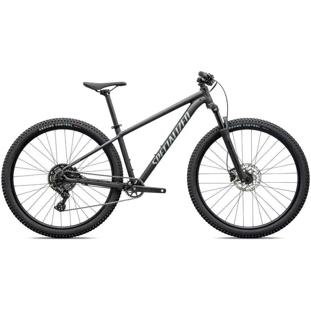 Gray mountain bike shown in a partial side view, highlighting the frame, large knobby tires, and front fork with disc brake outfits.