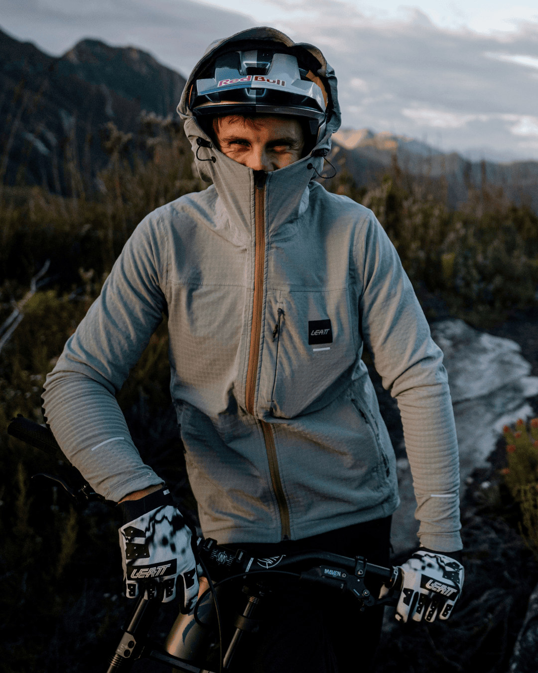 Cyclist wearing a gray Leatt jacket and helmet, with gloves, hands on the handlebars in a rocky alpine landscape