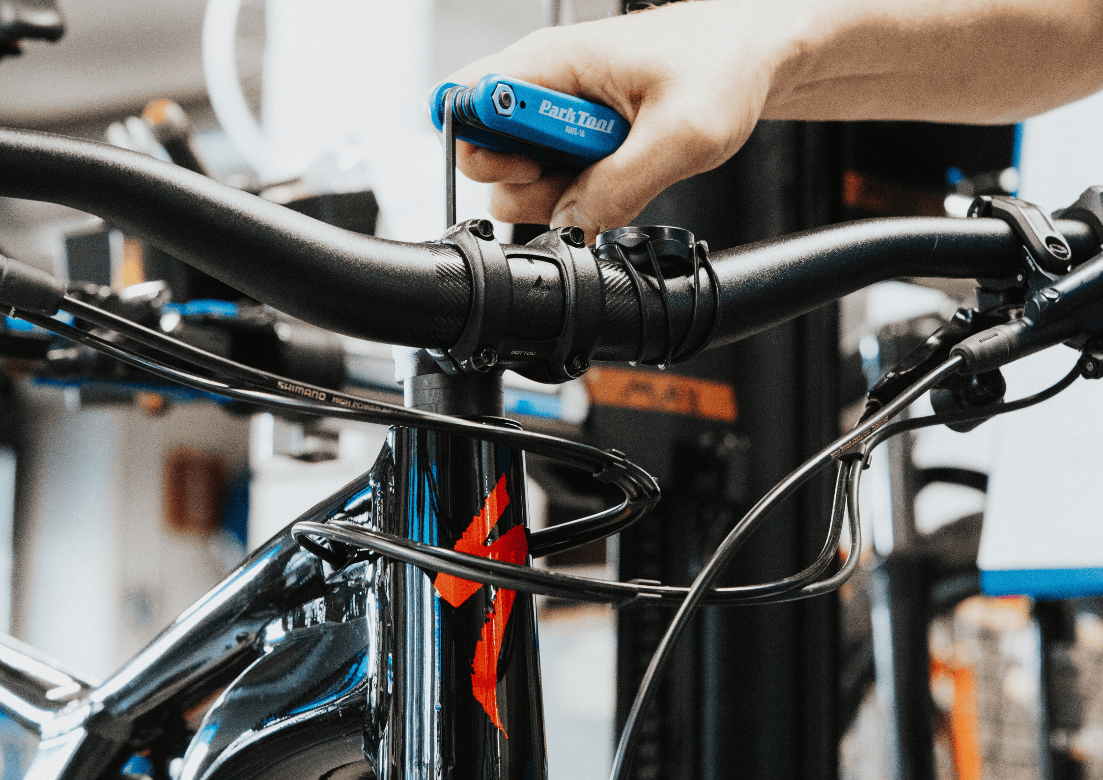 Person using a Park Tool hex wrench to adjust the handlebars on a glossy black bike frame in a workshop setting