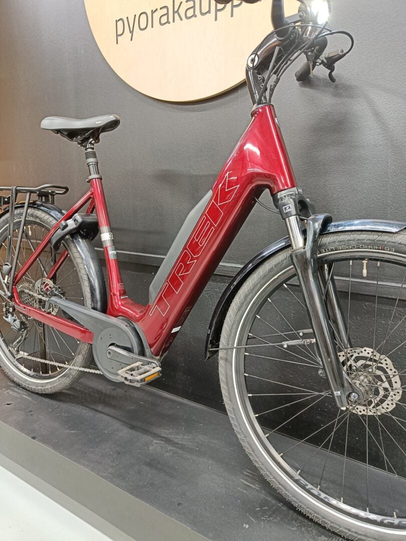 Red Trek electric bike with integrated battery on the downtube, front suspension, and rear luggage rack indoors.