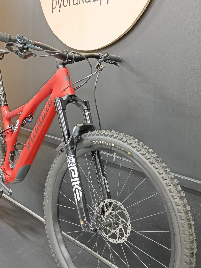 Red Specialized mountain bike indoors, front suspension fork, knobby tires, hydraulic disc rotor visible on front wheel