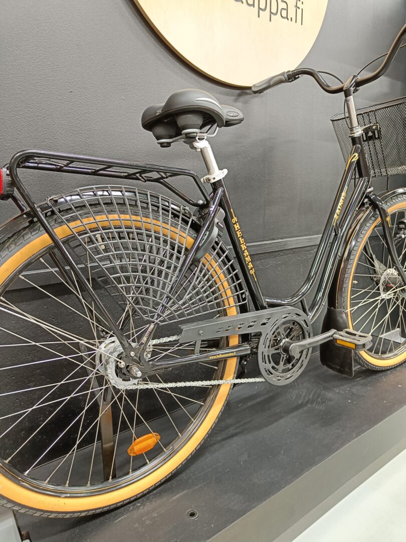 Black city bicycle with tan tires, rear cargo rack, and a front basket on display.