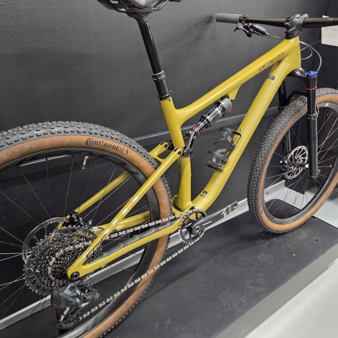 Yellow Specialized mountain bike on display, showing rear derailleur, chain, and knobby Continental tires in a showroom.