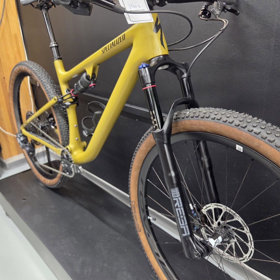 Yellow full-suspension mountain bike, close-up of front fork and frame with knobby tires in a showroom.