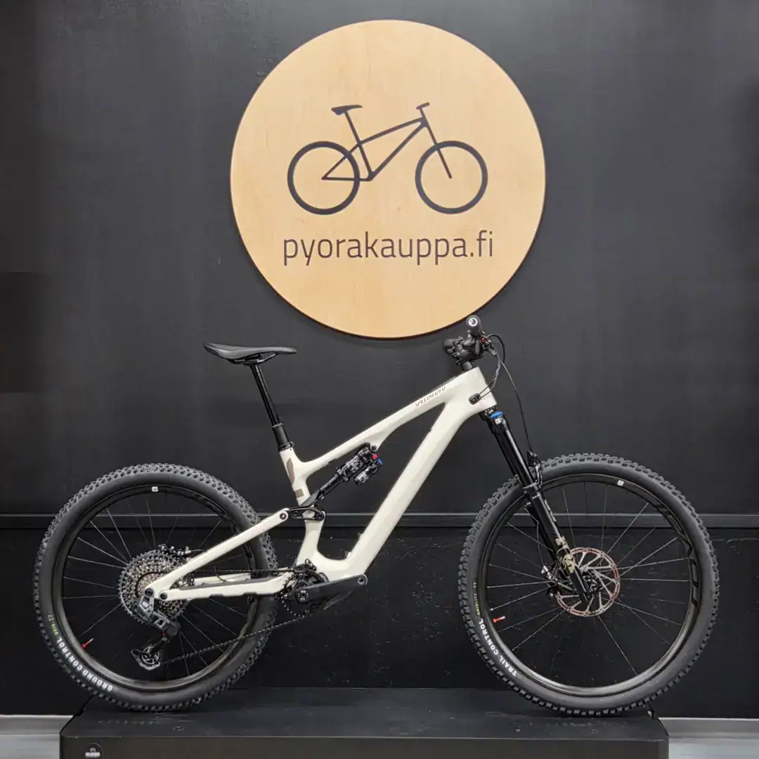 White full‑suspension mountain bike displayed on a dark wall beneath a circular wooden sign with a bicycle icon and the text 'pyorakauppa.fi'