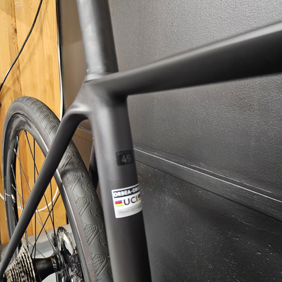 Close-up of a bicycle's front fork and tire, with a sticker visible on the fork near a dark wall in indoor setting.