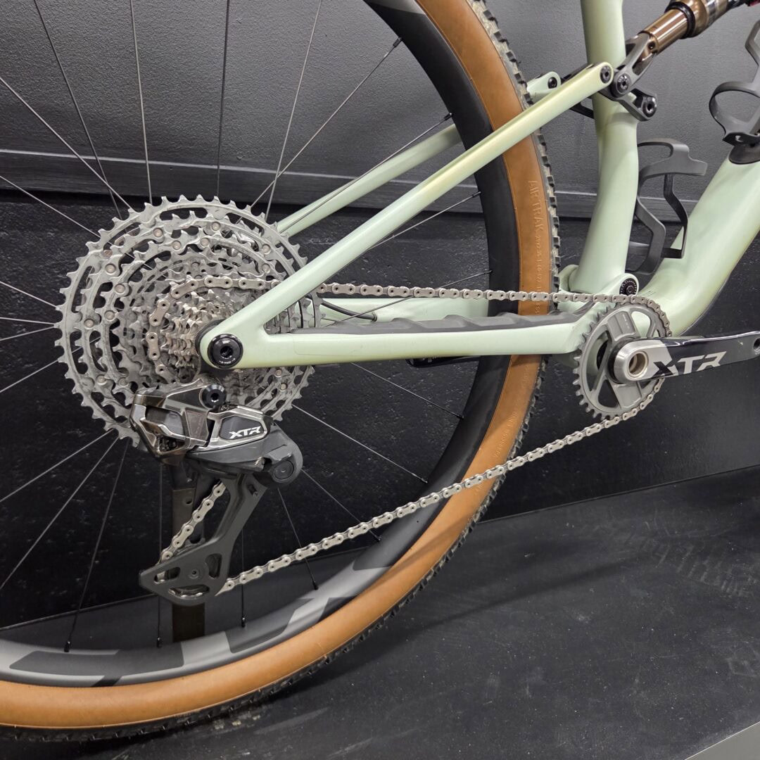Close-up of a mint green bicycle frame showing rear drivetrain, cassette, chain, and tan-wall tire on a dark background.