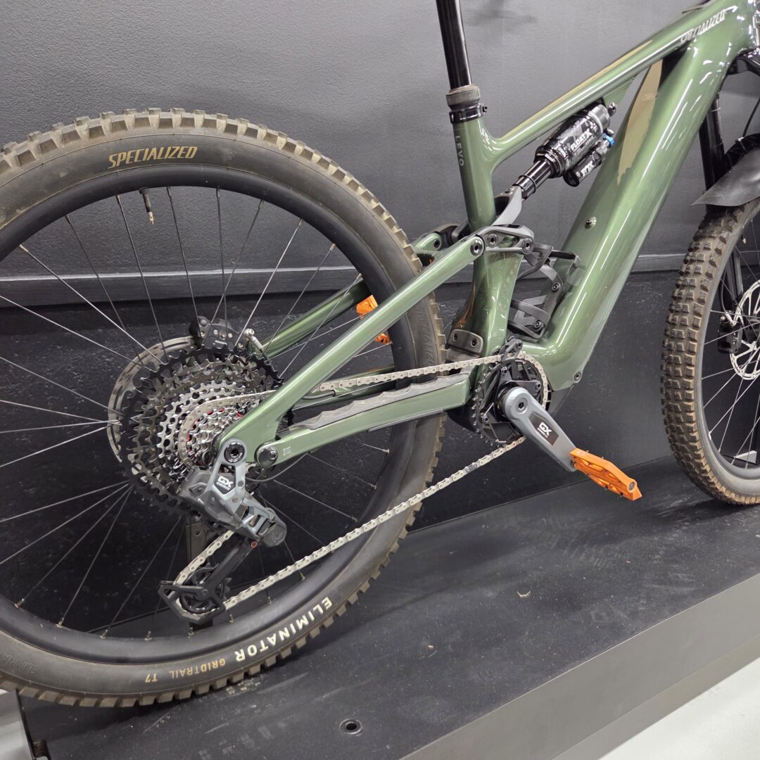 Green full-suspension mountain bike close-up of the rear wheel, drivetrain, and frame with a Specialized tire label visible on the rim.