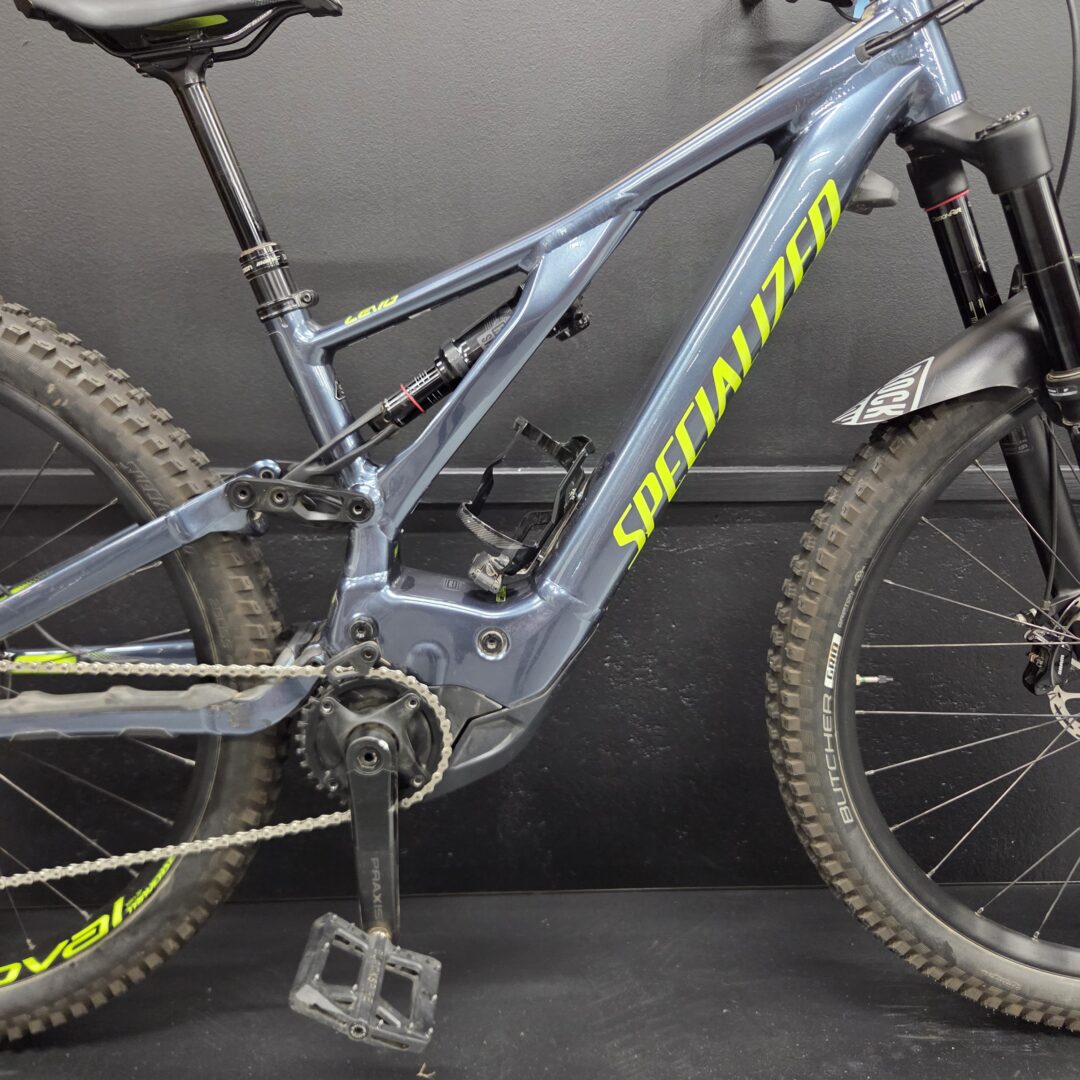 Blue mountain bike frame with bright yellow 'Specialized' lettering, showing crankset, chain, pedals, and front suspension fork.