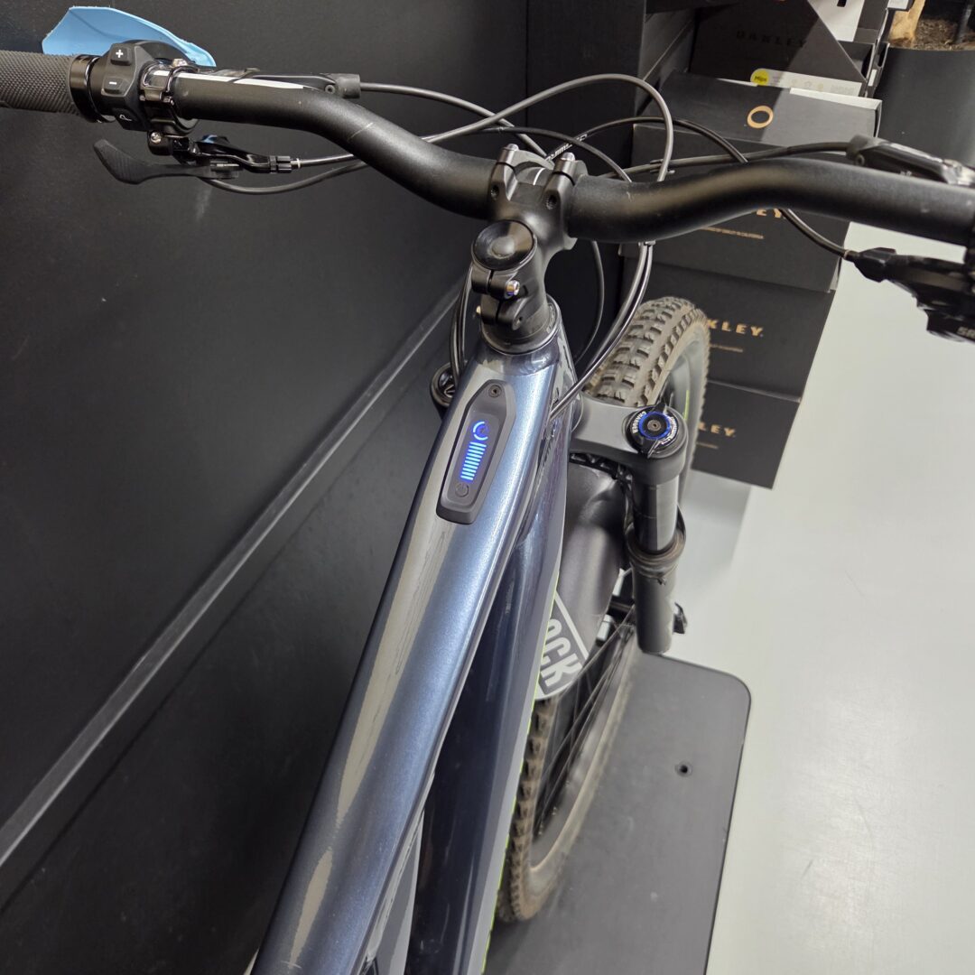 Close-up of an electric bike handlebar with brake levers, cables, and a blue-lit control panel on the frame.