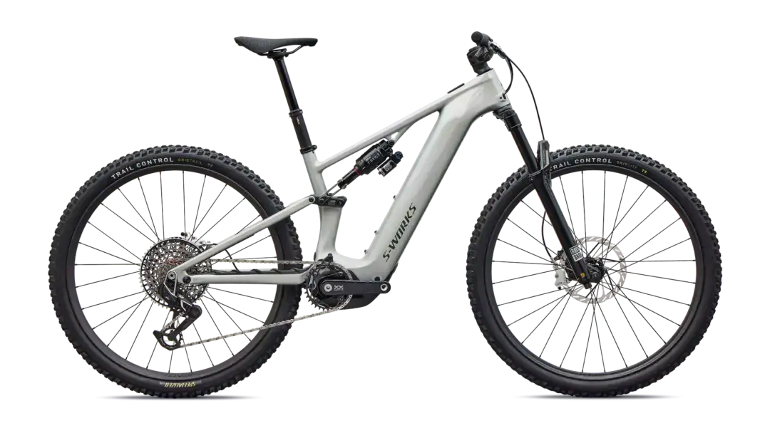 Full-suspension mountain bike with a light gray frame, large knobby tires, disc brakes, and dropper seatpost labeled 'S-Works'