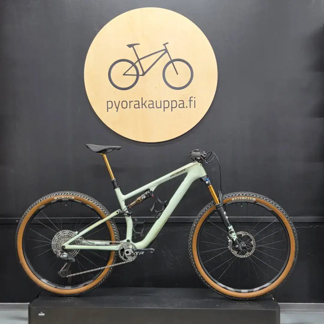Mint green mountain bike mounted on a black wall beneath a round wooden sign that reads 'pyorakauppa.fi'.