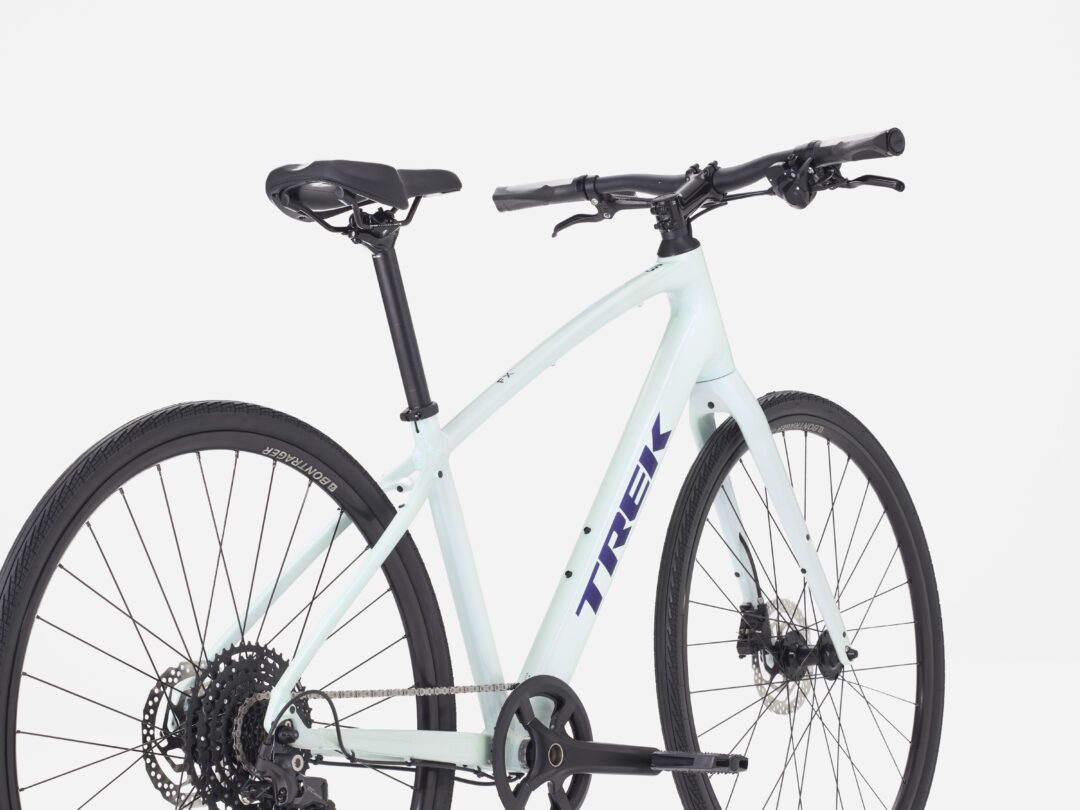 Close-up of a light blue bicycle frame showing the saddle, handlebars, and drivetrain with visible gears and disc brakes.