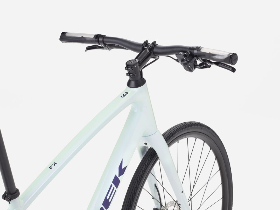 Mint green bicycle frame with black handlebars, brake levers, and a visible front wheel against a light background as a close-up cockpit view.