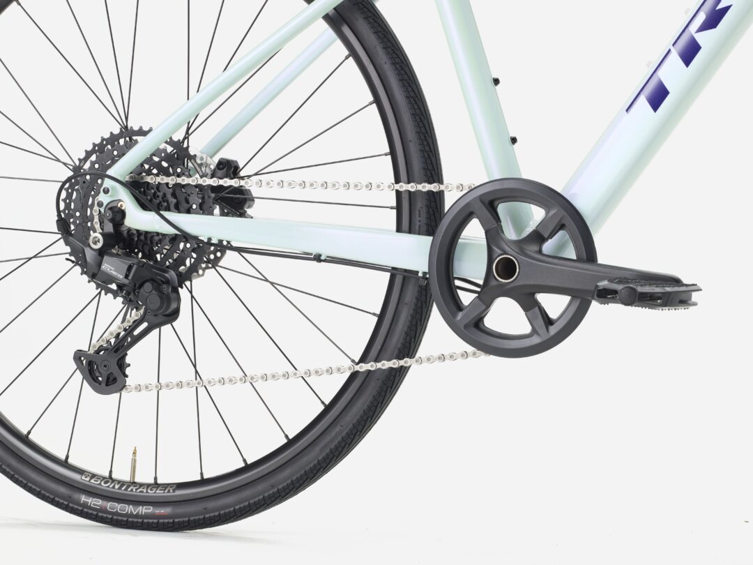 Rear drivetrain of a light-colored bike: cassette, chain, derailleur, and crank visible