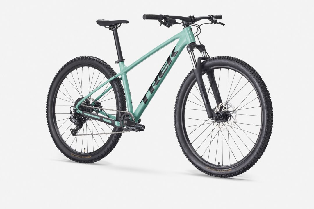 Teal hardtail mountain bike with front suspension, wide knobby tires, and black saddle against a white backdrop.