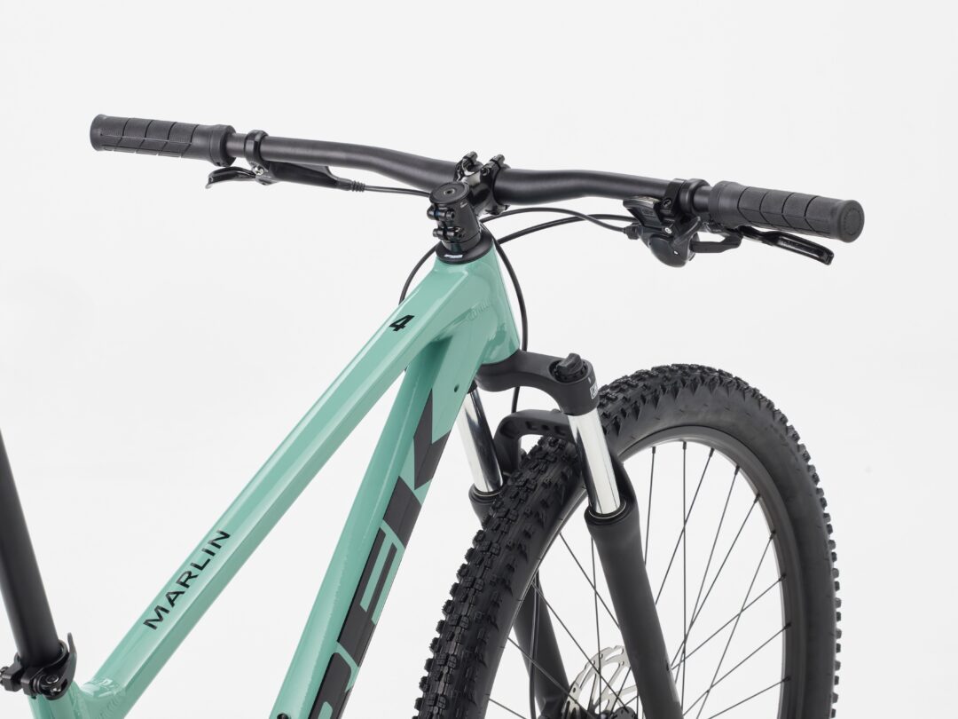 Close-up of a turquoise-green mountain bike showing the handlebars, grips, and front wheel with knobby tires.