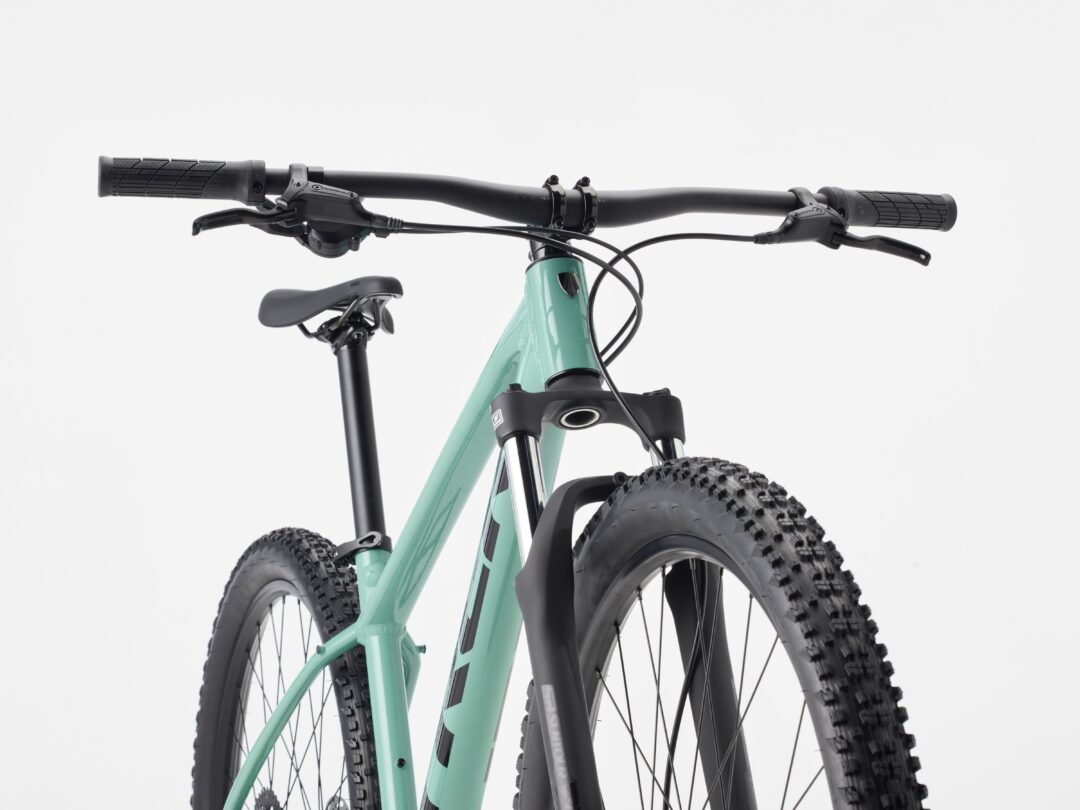 Front view of a teal mountain bike showing handlebars, grips, and large knobby tires.