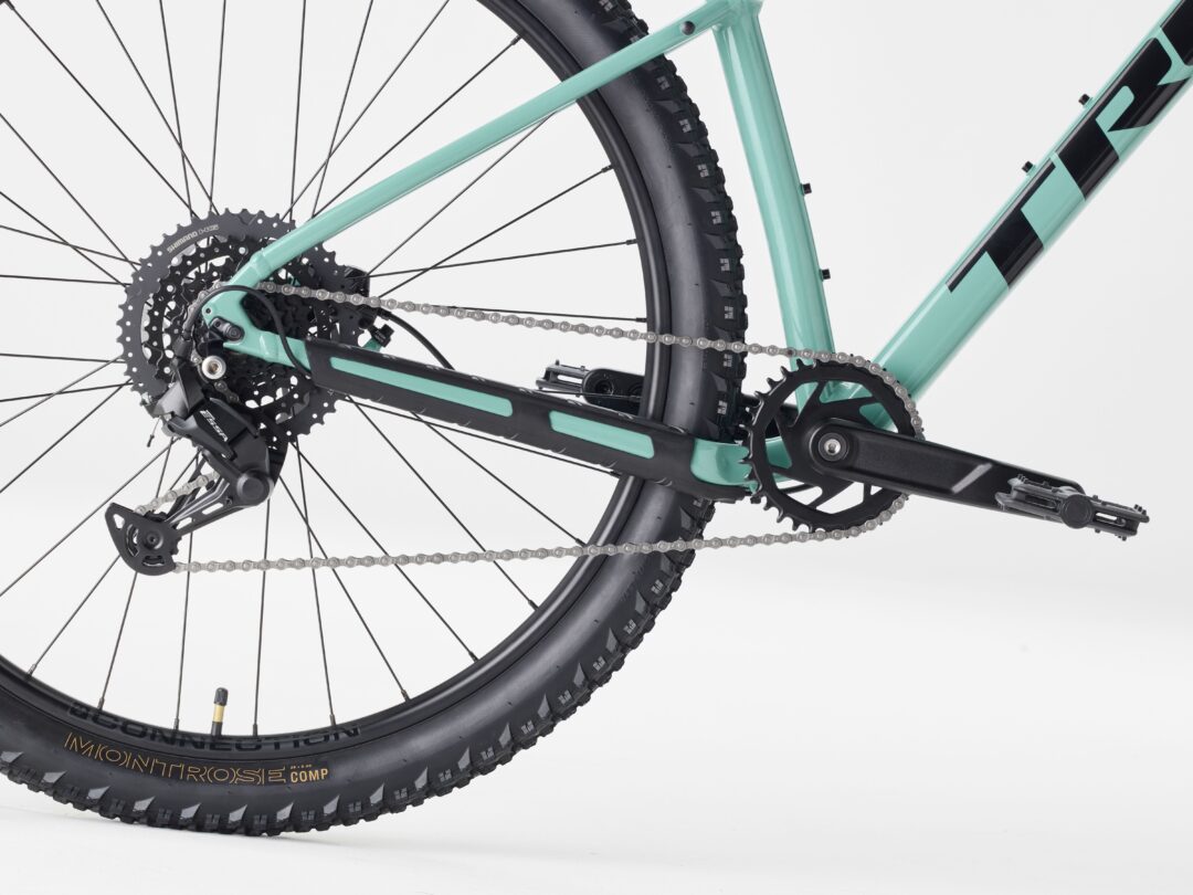 Close-up of the rear wheel and drivetrain of a mint-green mountain bike, showing the cassette, chain, derailleur, and knobby tire.