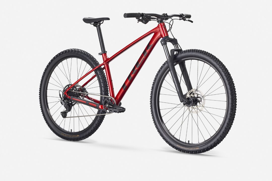 Side view of a red mountain bike with wide knobby tires, front suspension, and disc brakes on a white background