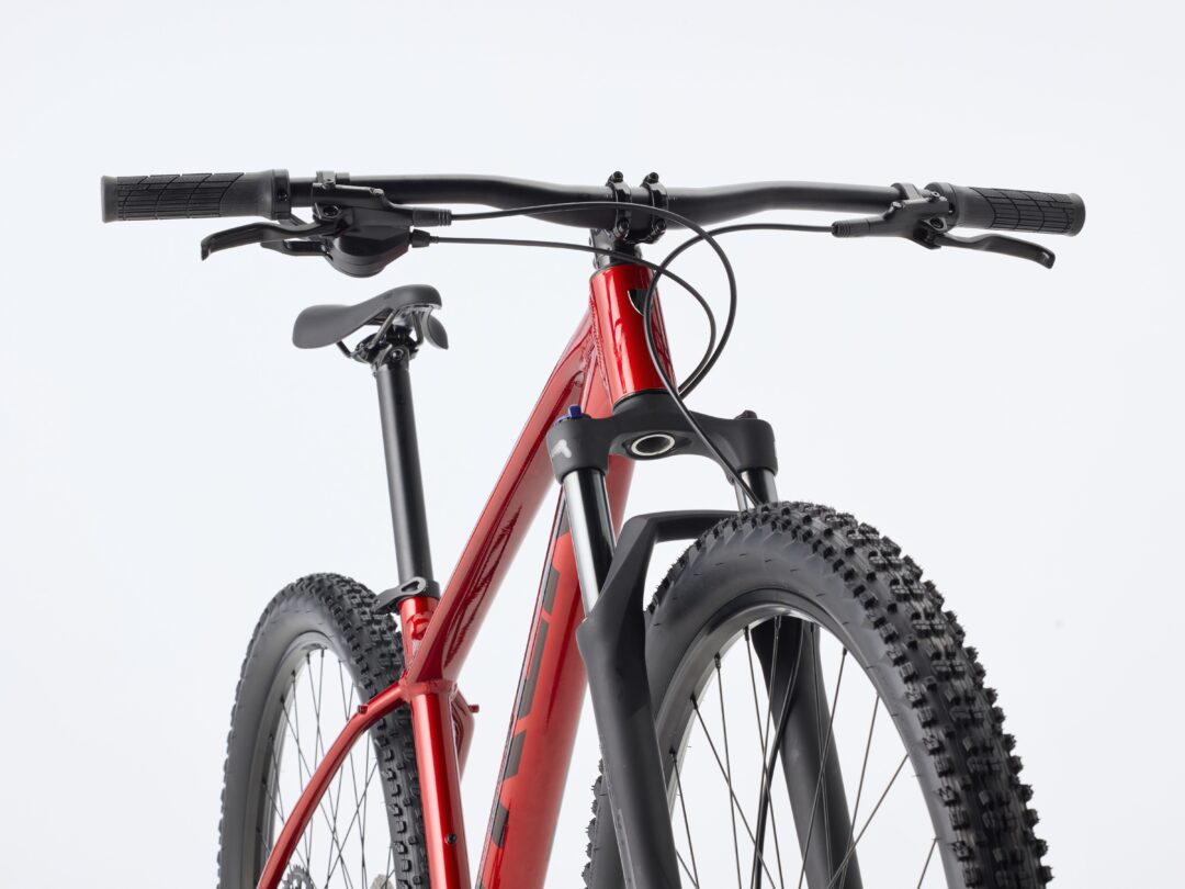 Close-up of a red mountain bike front end with black handlebars, brake levers, and chunky tires.