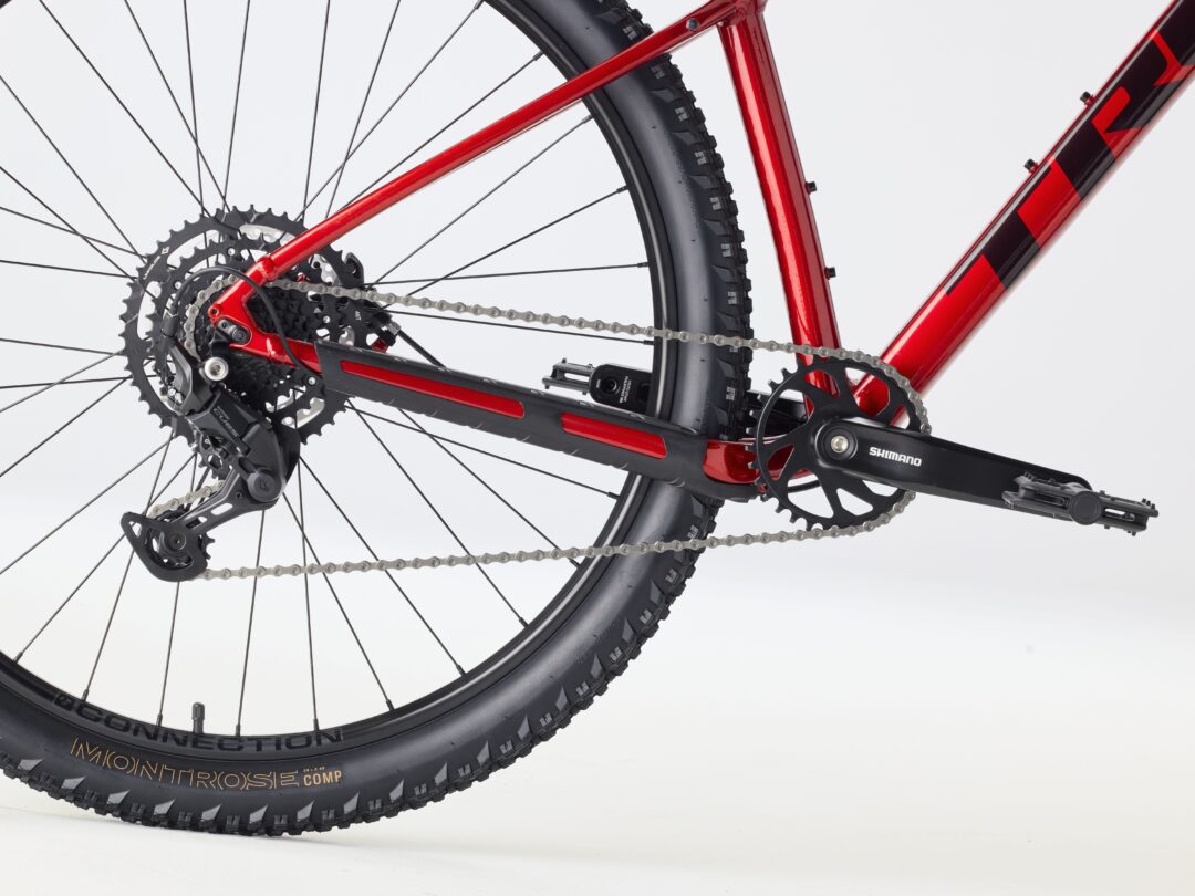 Close-up of a red bicycle frame around the rear wheel, showing the gears, chain, derailleur, and tire with Shimano crank visible in the foreground.