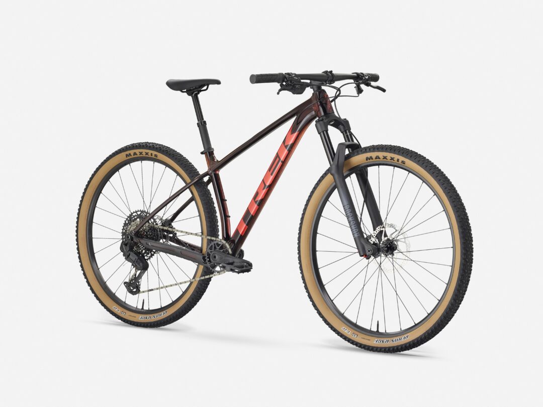 Partial side view of a black mountain bike with tan tires and red accents against a white backdrop.