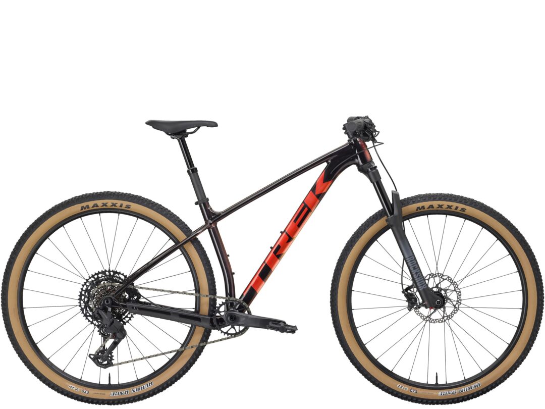 Mountain bike with black frame and red accents, showing both wheels and drivetrain (Maxxis tires with tan sidewalls)