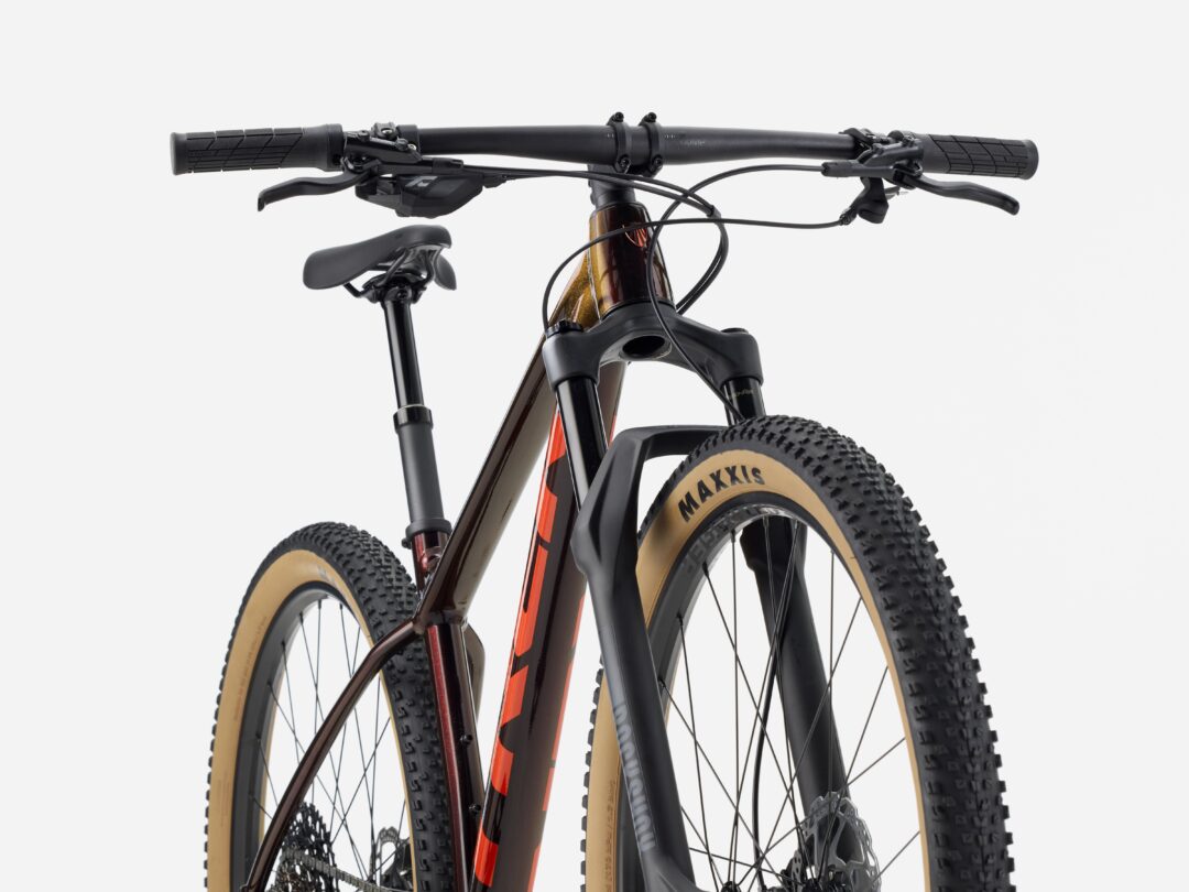 Front view of a mountain bike: wide flat handlebars, brake levers, cables, and tan-wall tires with a suspension fork.