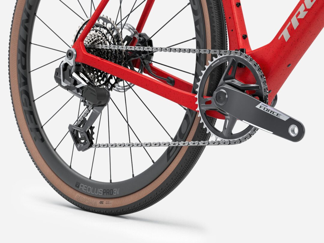 Close-up of a red road bike's rear drivetrain: derailleur, cassette, chain on the rear sprockets, with SRAM Force components and a tan-sidewall wheel tire.