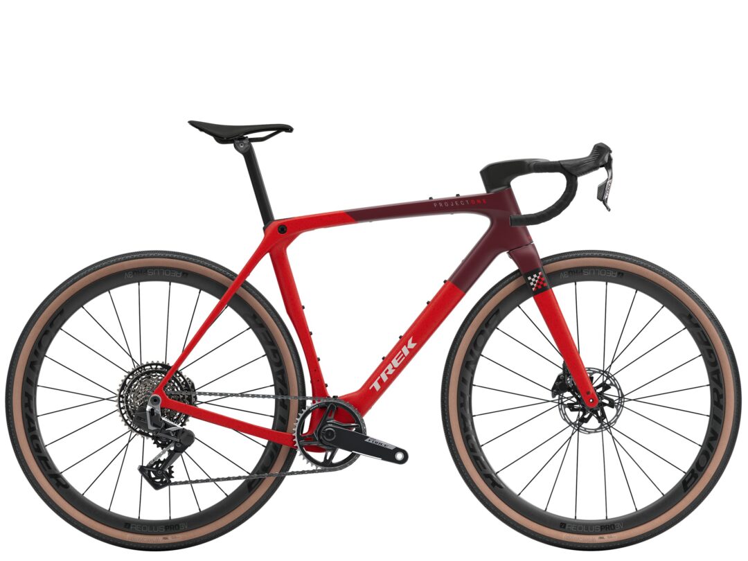 Partial view of a red and maroon Trek Project One road bike with black drop handlebars and tan-wall tires.