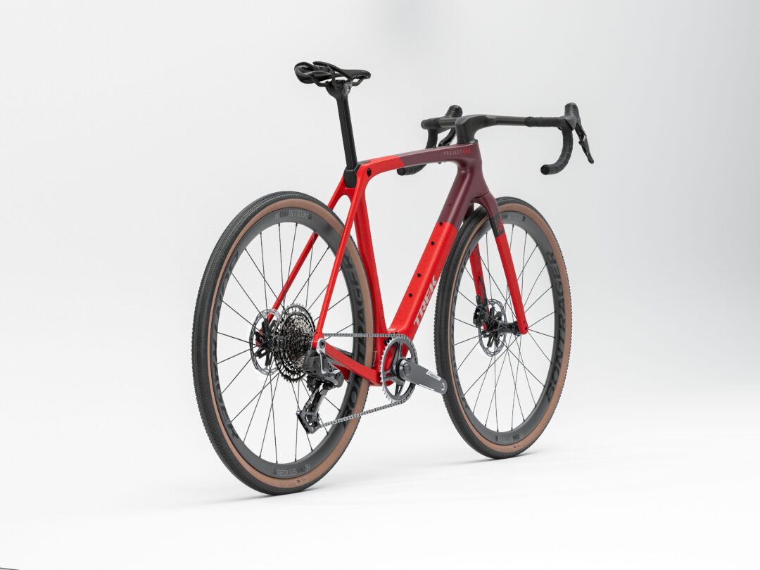 Red carbon road bike with drop handlebars and tan-wall tires posed on a white studio backdrop.