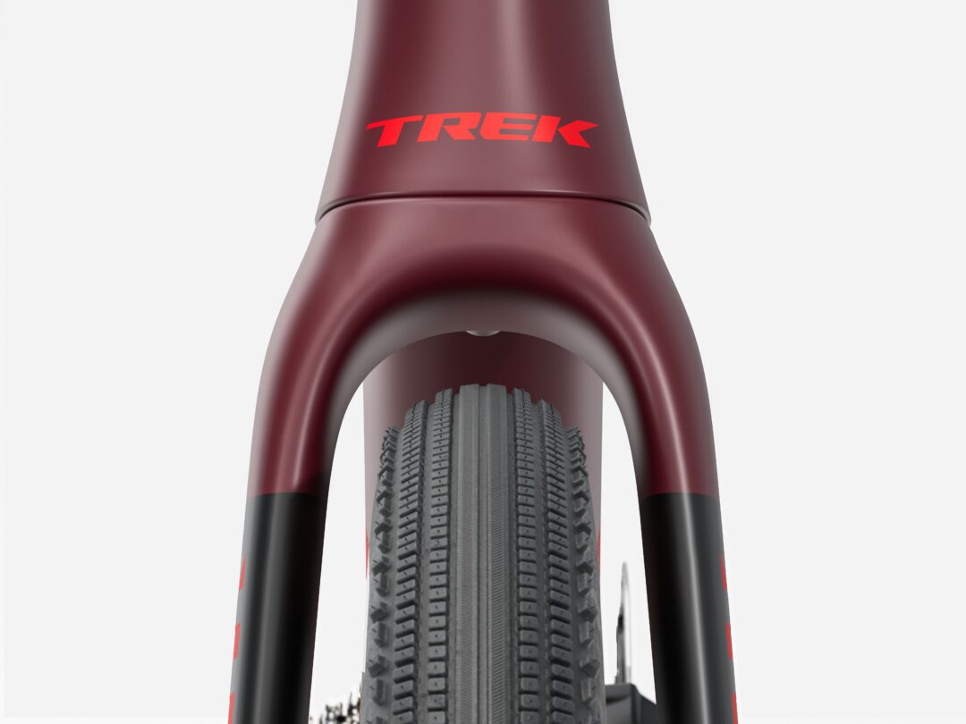 Close-up of a maroon Trek bicycle frame around a tire, highlighting the red Trek logo at the head tube area.