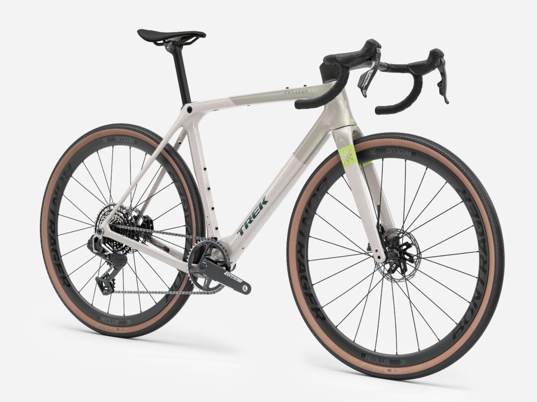 Side view of a silver-gray road bike with drop handlebars, black saddle, tan-wall tires, and Project One branding on the frame