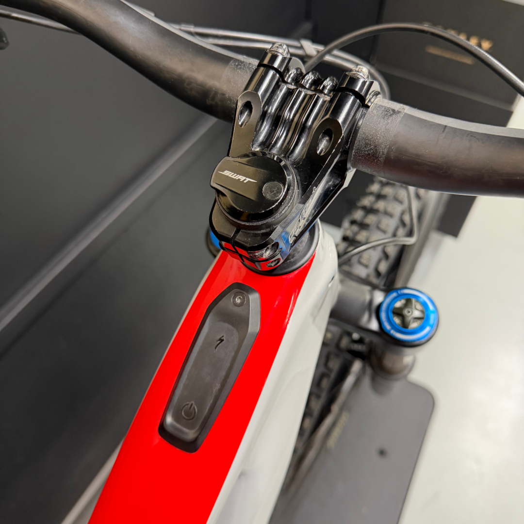Close-up of a mountain bike's front end: stem, headset bolts, and red frame tube with cables nearby