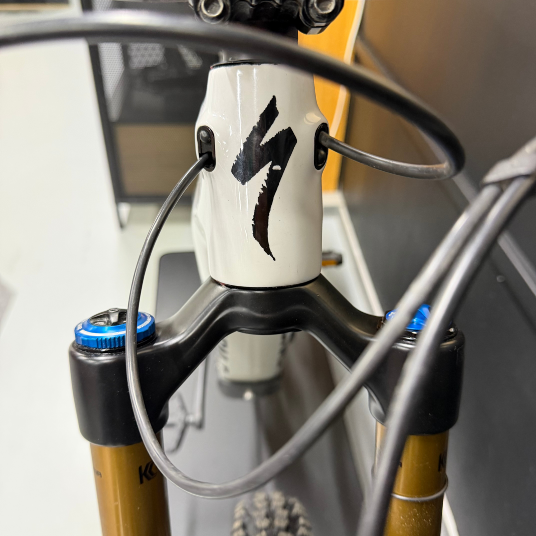 Close-up of a bicycle head tube with peeling sticker, front cables, and gold-colored suspension forks.