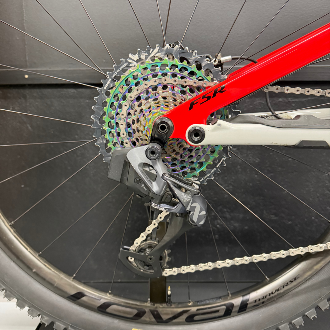 Close-up of bicycle rear derailleur, rainbow cassette, and chain on a red frame.